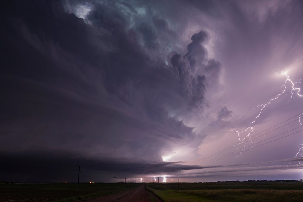 Lightning strikes from a tornado-producing supercell thunderstorm over a rural dirt road and open grassy landscape, Storm Chasing, Lisbon, North Dakota, USA.