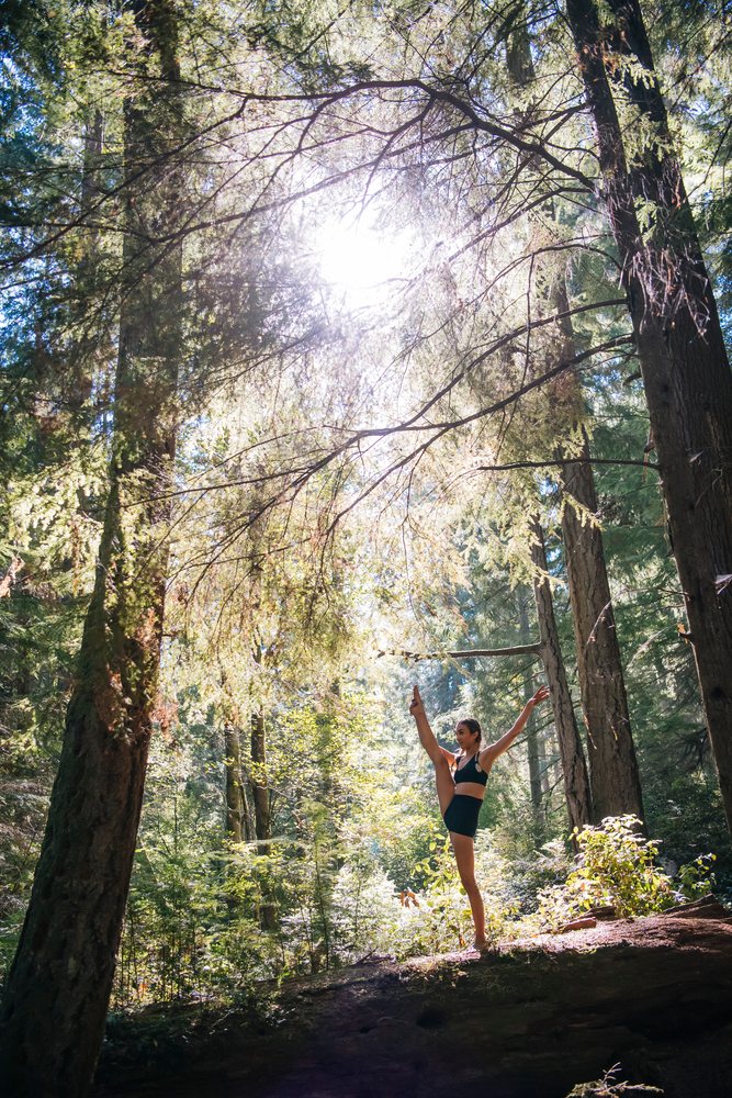 Woman stretches her leg high and balances in a sunlit forest, contortionist, Tacoma, WA, USA.