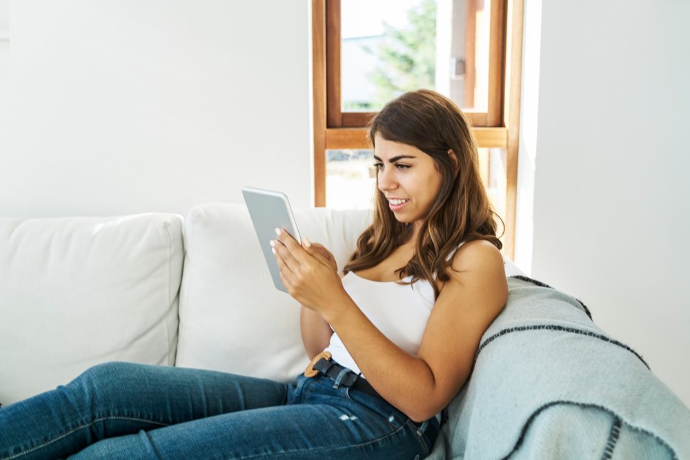 A white woman using a tablet while relaxing on a couch