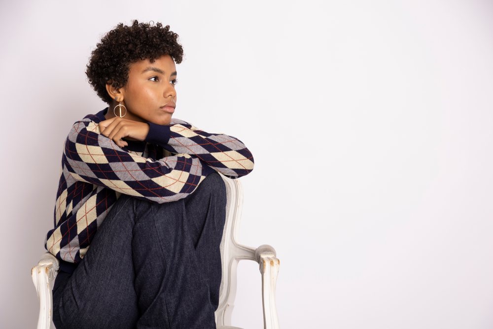 Young woman seated on a white chair looking thoughtfully to the side against a plain white studio background, fashion, young culture.