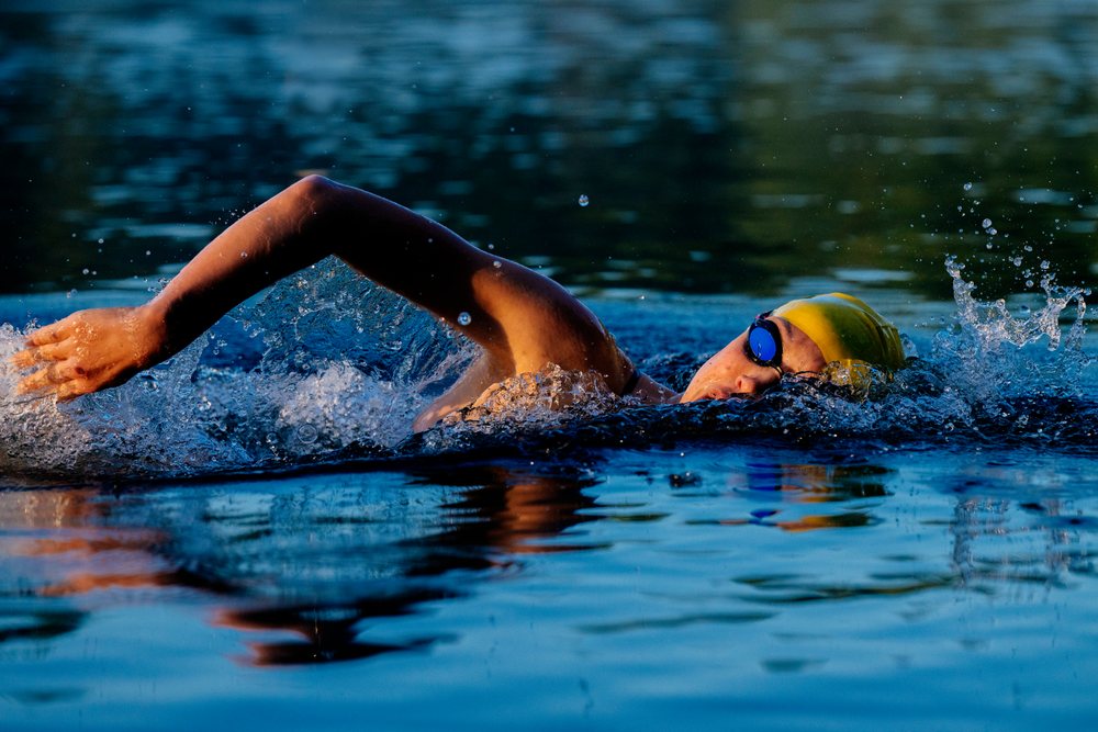 Swimmer wearing a yellow swim cap and goggles performing the front crawl stroke in open water, USA.