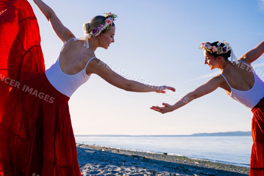 Two white women practicing partner acrobatics yoga on a beach