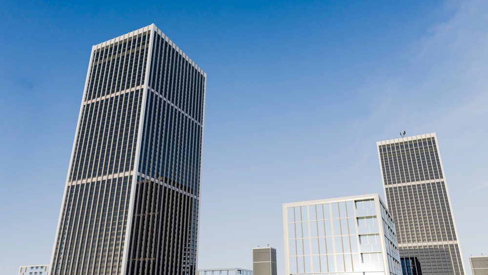 Multiple modern skyscrapers with glass facades reflect clear blue sky in a city business district during daytime.