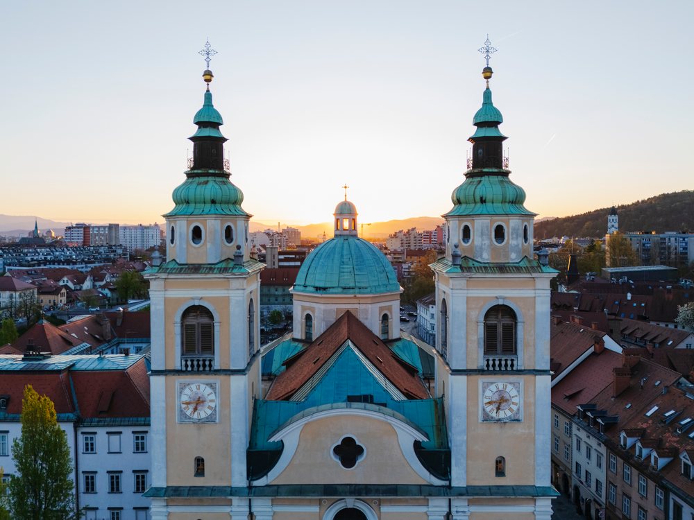 St Nicolas Cathedral with twin towers and central green dome at sunset overlooking Ljubljana cityscape, Slovenia.