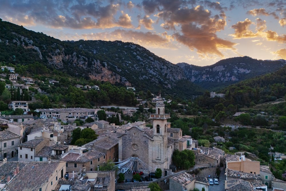 Sunrise over Valdemossa village, showing historic stone church and rooftops with mountain range backdrop, Landscape, Lifestyle, Mallorca, Spain.