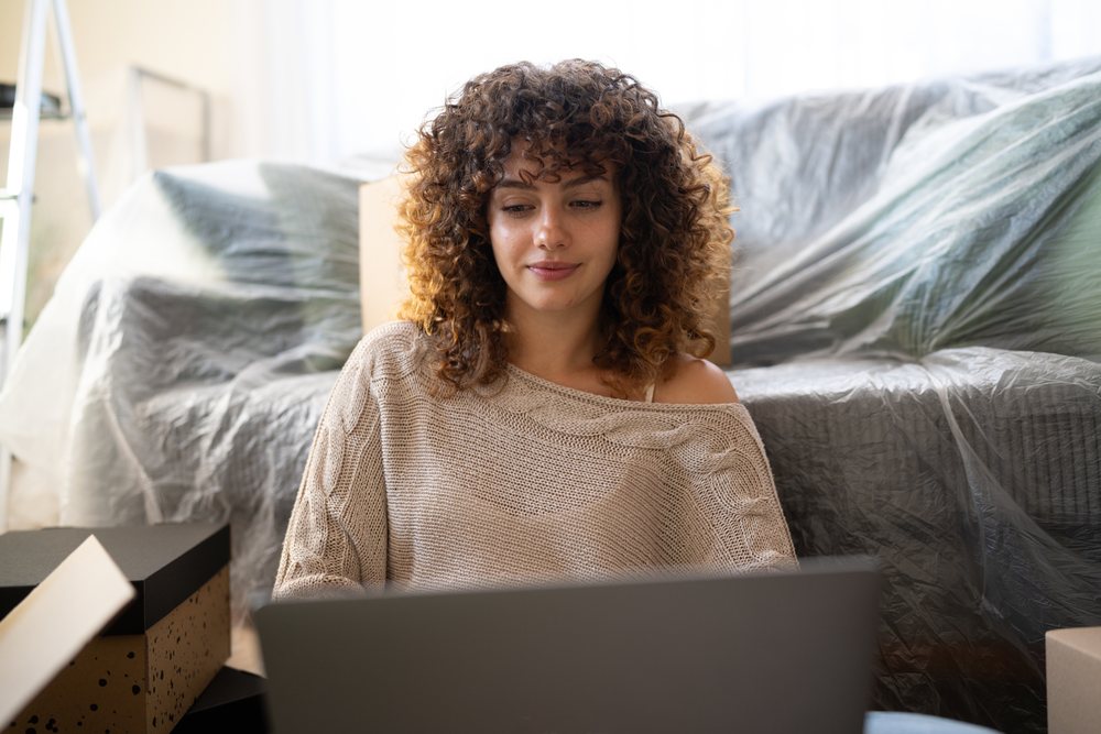 Woman with curly hair using a laptop while sitting on the floor, moving, Spain.
