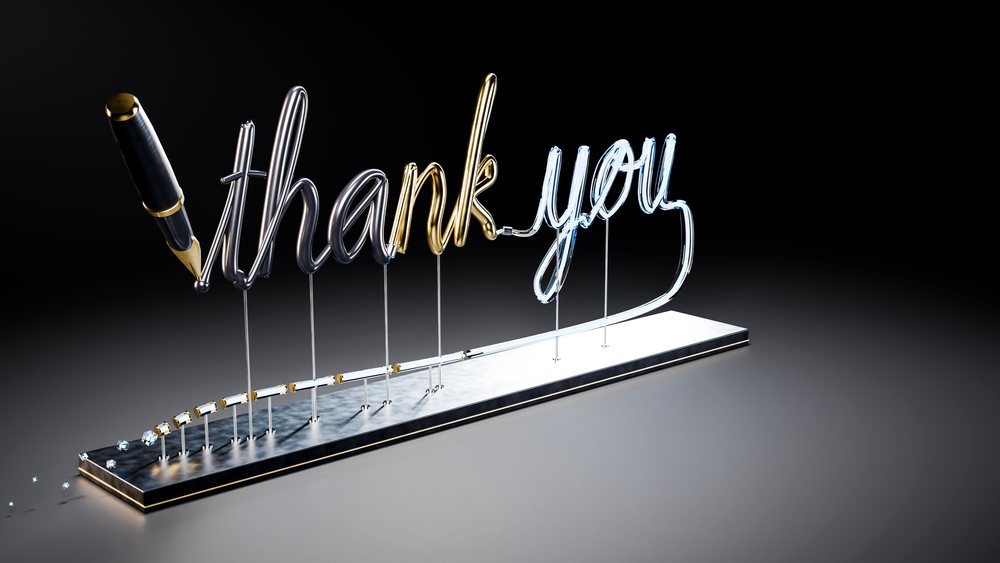 Metallic script spelling thank you with pen tip on metal stand against black background.