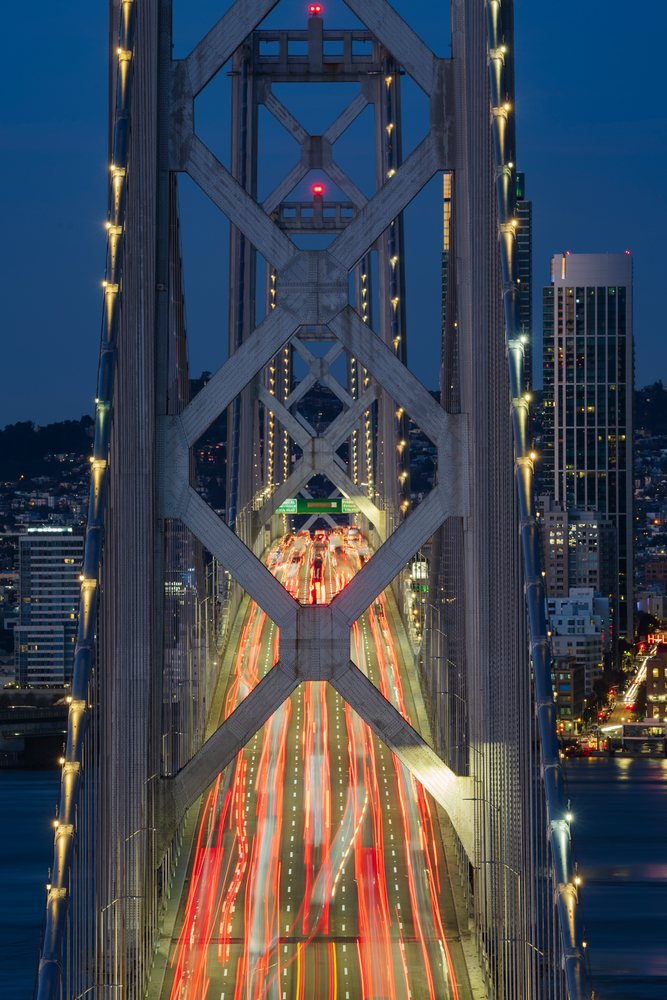 Multiple lanes of vehicular Traffic move across the illuminated steel suspension Bay Bridge at Dawn with the city skyline in the background, Cityscapes, City Life, San Francisco, California, USA.