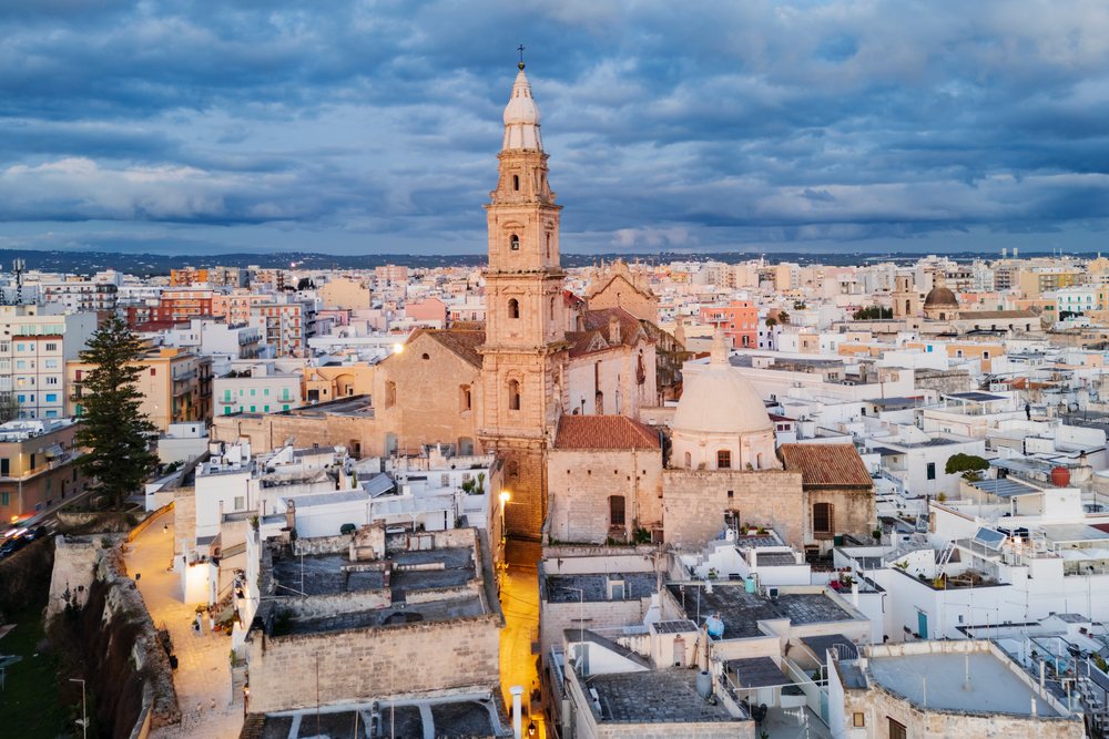 Historic stone Cathedral Basilica of Maria Santissima della Madia with bell tower and dome amid Monopoli cityscape at dawn, Puglia, Italy.