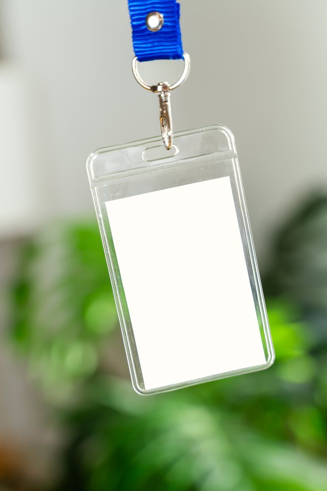 Blue fabric lanyard with metal clip holding a clear plastic badge holder containing a white card against a blurred green background, mock up, white screen, Spain.