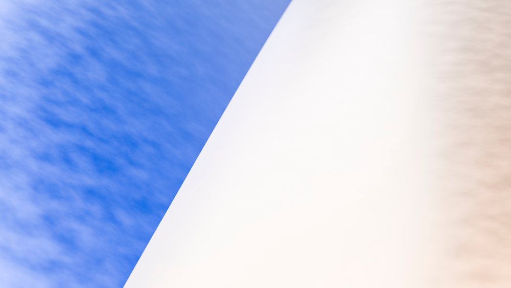 White curved architectural structure stands against a bright blue sky dotted with clouds on a clear day.