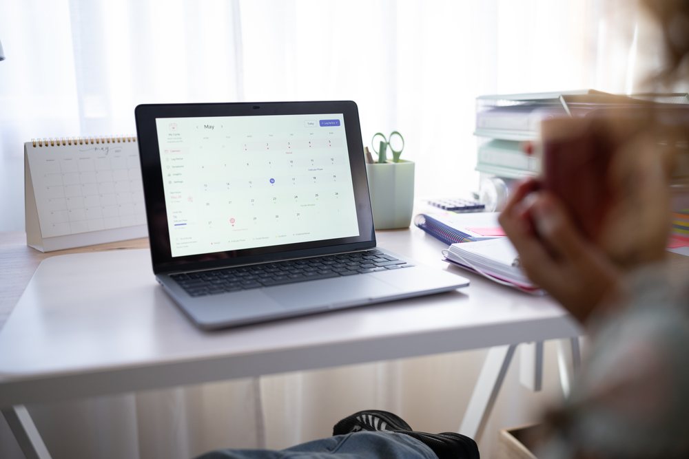 Laptop screen shows a calendar next to a desktop calendar on a desk with notebooks and scissors in a pen holder indoors, home, girl, Spain.