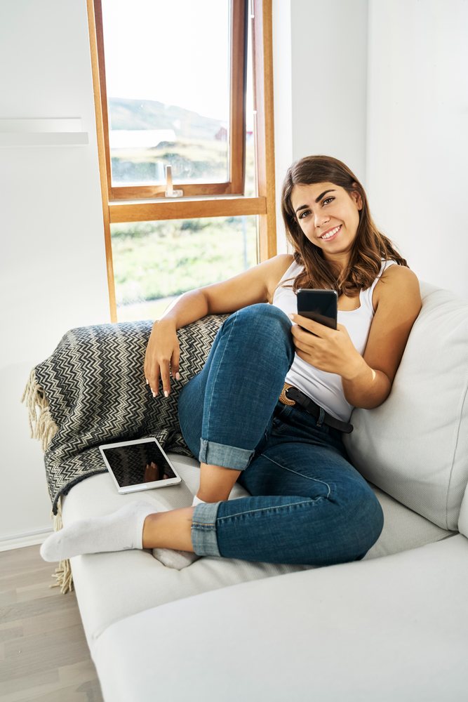 Young white woman relaxing on couch using smartphone