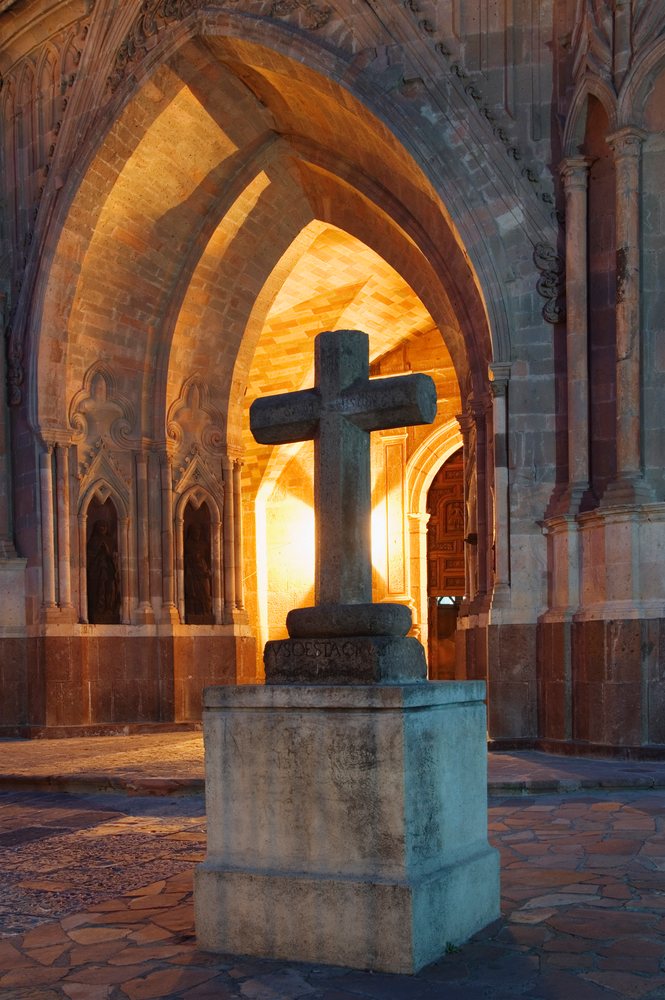 Stone cross monument on a stone pedestal beneath an arched stone architecture, San Miguel de Allende, Mexico.