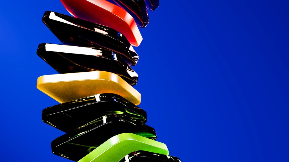 Stacked colorful abstract plastic shapes sculpture with shiny reflective surfaces against a blue background in a studio setting.