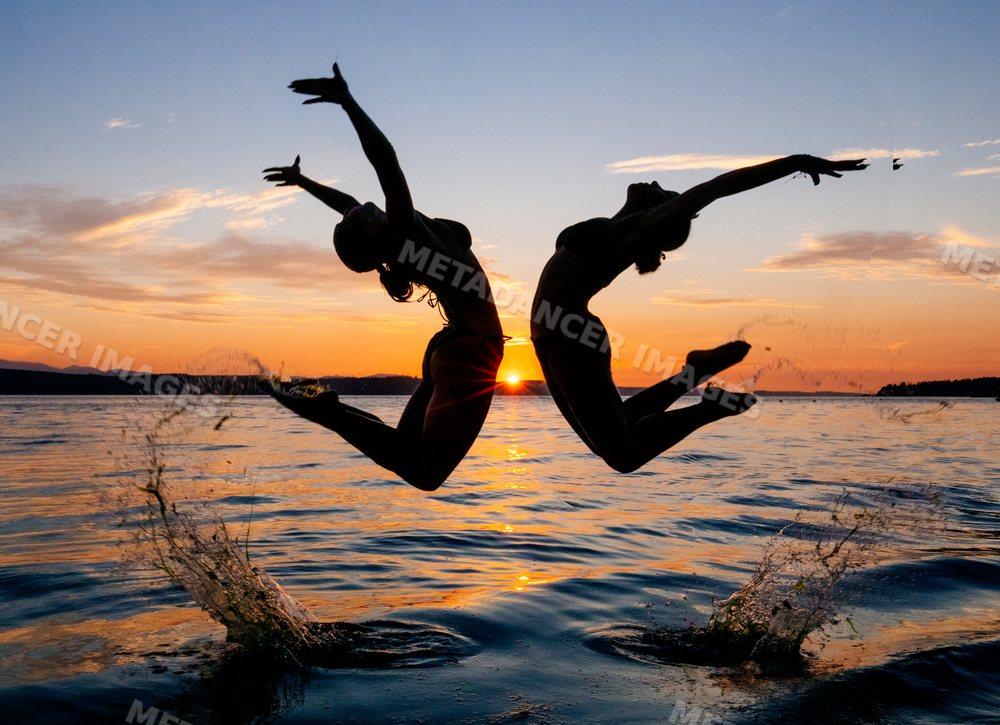 Two women practice partner yoga acrobatics leaping from water