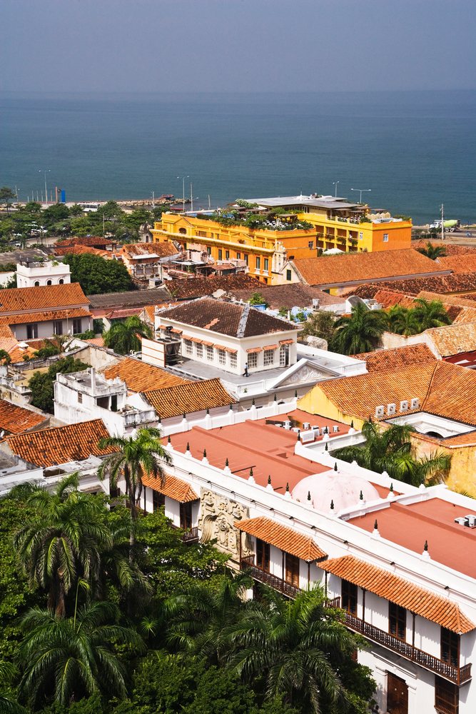 Old town Cartagena rooftops with red tile roofs and palm trees along the Caribbean coast under a clear sky, Colombia.