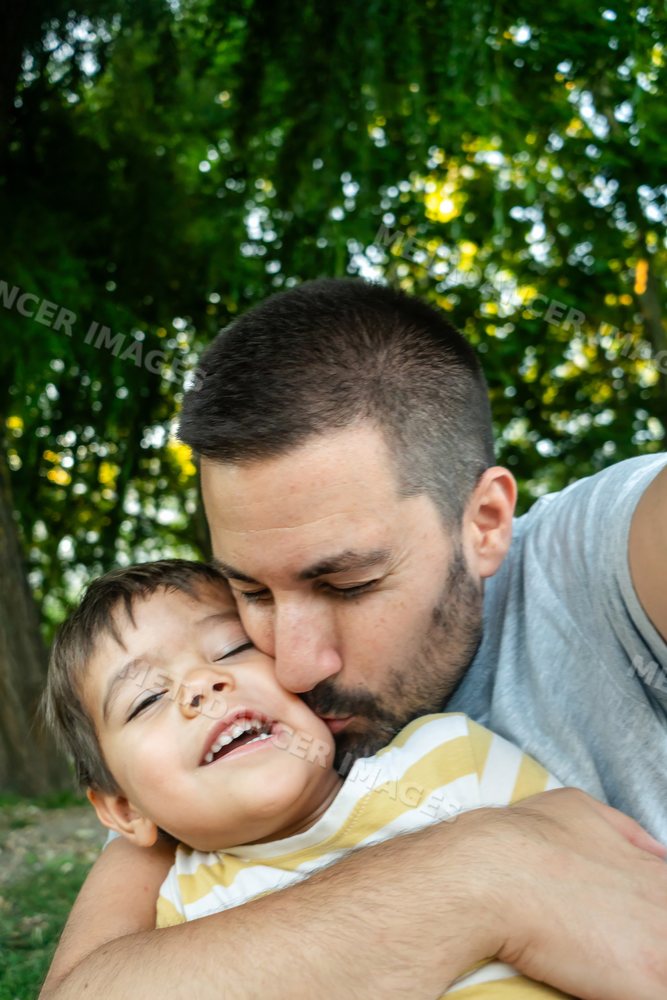 Father lovingly embraces and kisses his smiling young son outdoors