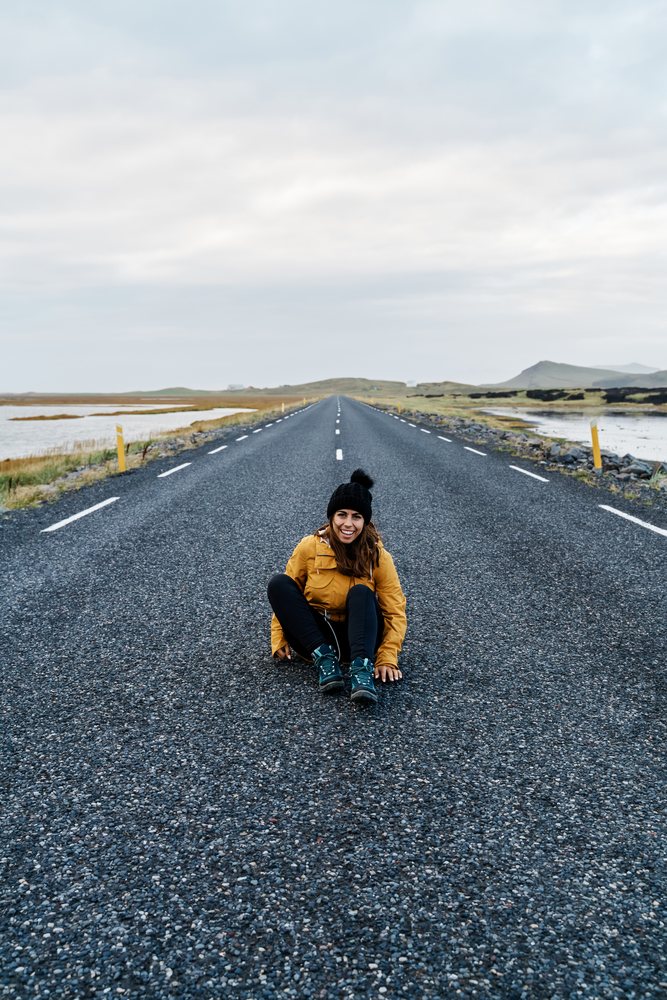 A white woman sitting and smiling on an empty road