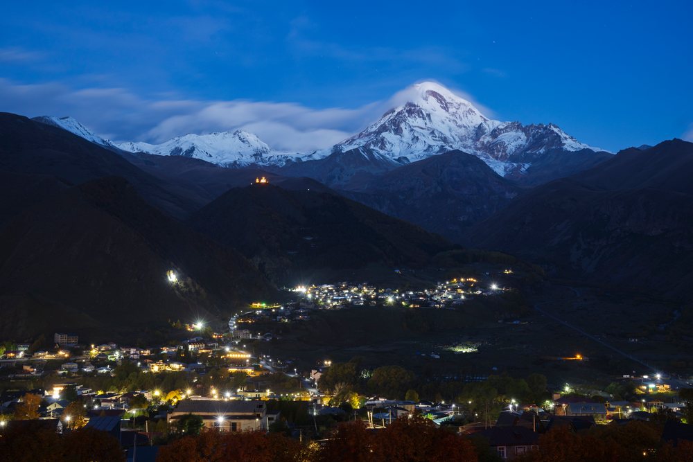 Stepantsminda village illuminated at Dawn with snowcapped Mt Kazbegi towering in the background, Georgia.