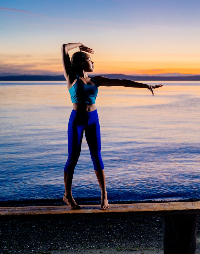 Woman stretching and balancing on a wooden beam near a lake at sunset, yoga, acrobatics, USA.