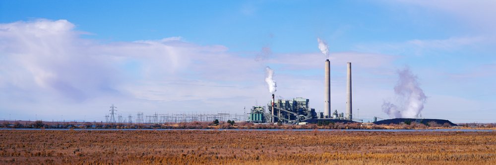 Coal fired power station with two tall smokestacks emitting steam and electricity pylons across an open field under blue sky, New Mexico, USA.