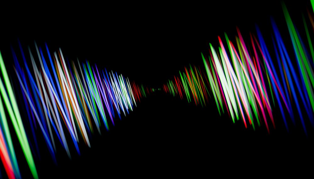 Symmetrical colorful light trails glow and blur against a dark background forming an abstract digital tunnel pattern.