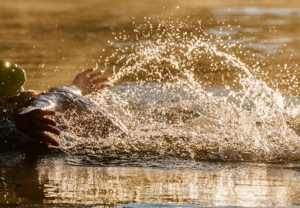 Swimmer creating a dynamic water splash during an active stroke in open water at golden hour, USA.