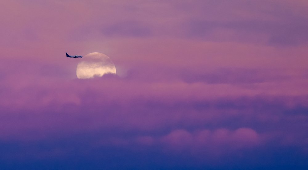 Aircraft flying in front of a full moon during twilight with purple clouds in the sky over the, USA.
