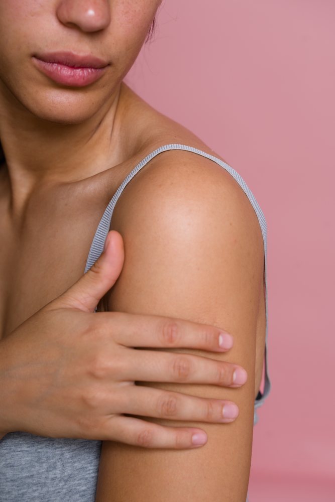Woman touching her shoulder, showcasing smooth, skin against a pink background in a beauty shoot, Spain.