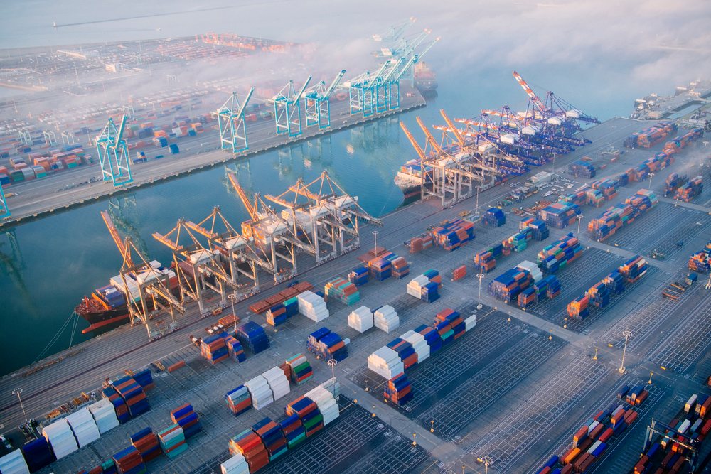 Container terminal at the port with cranes and stacked shipping containers along the dockside in morning light, the port, CA, USA.