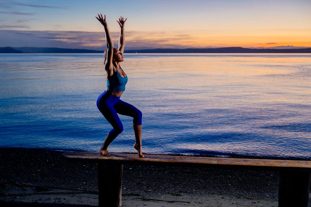 Woman performing a yoga balancing pose on a bench by a lake at sunset, USA.