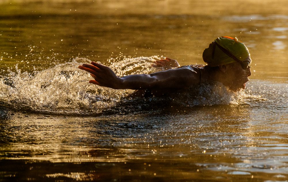 Athlete performing the butterfly swimming stroke in open water during golden light, USA.
