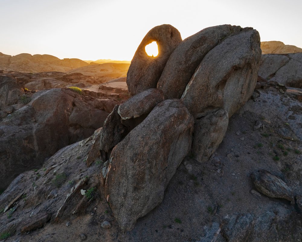 Sunrise light passes through a natural arch hole in a rock formation, landscape, wildlife, Purros, Kunene Region, Namibia.