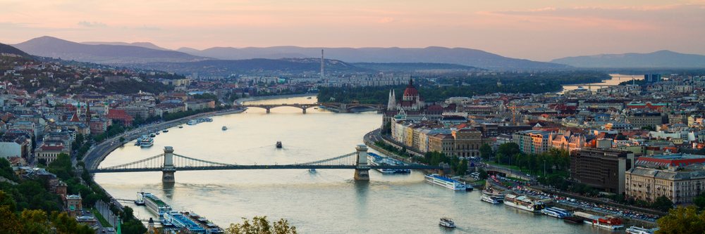 Panoramic view of the Danube River flowing through Budapest at sunset with multiple bridges and the Parliament building along the riverbank, Hungary.
