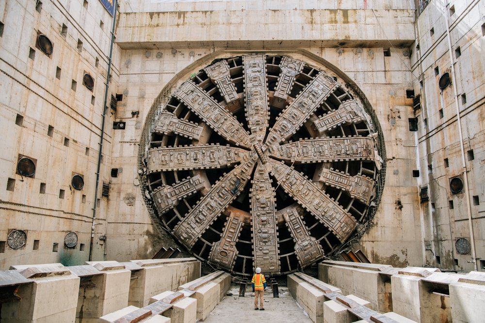A construction worker stands in front of a large tunnel boring machine inside an underground tunnel construction site, a large tunnel boring machine, drilling, USA.