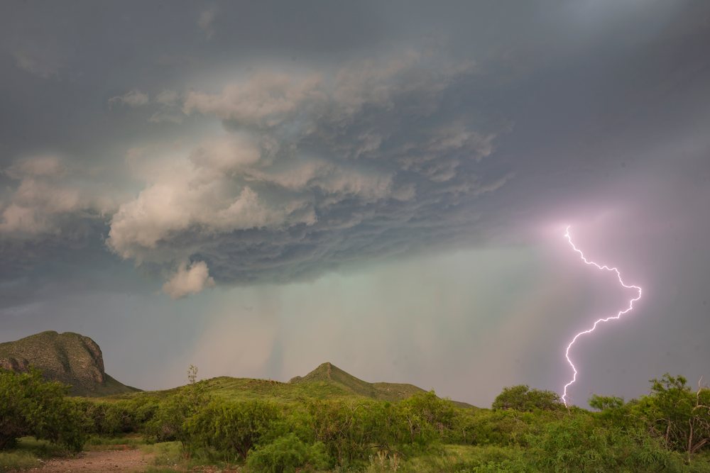 Lightning bolts strike the ground amid a thunderstorm over green hills and desert vegetation, Storm Chasing, Weather, Environmental Issues, USA, Arizona.