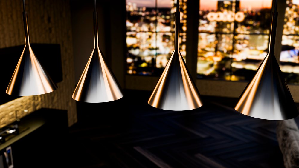 Four modern cone-shaped pendant lights with metallic finish illuminate a dark room showing a blurred night cityscape through the window.