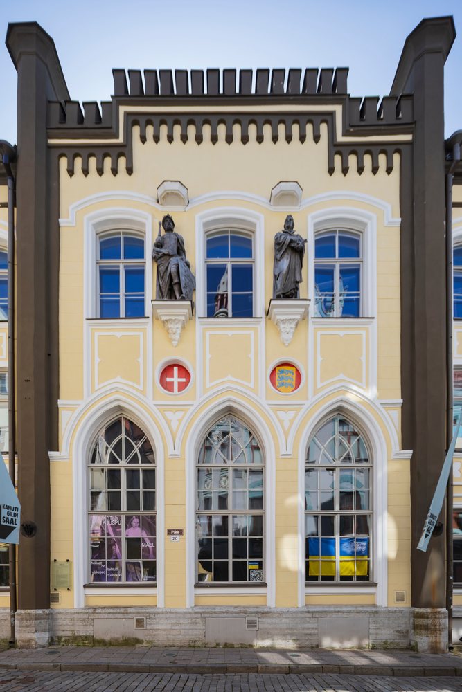 Facade of Canute’s Guild Hall on Pikk 20, showing yellow walls, arched windows, statues, and a flag in a historic cityscape, Tallinn, Estonia, Baltic States.
