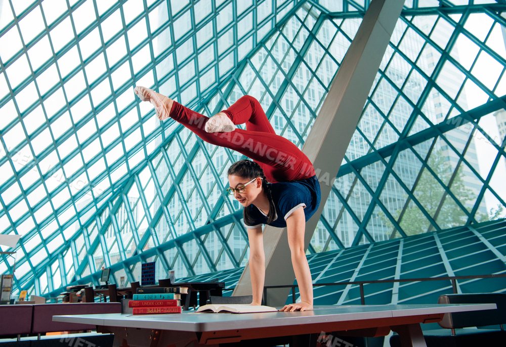 A young woman practices a handstand yoga pose on a table in a library