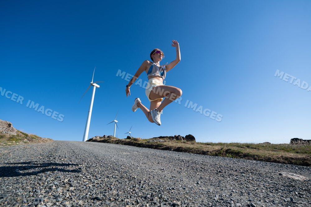 A white woman jumping outdoors near wind turbines in Galicia, Spain