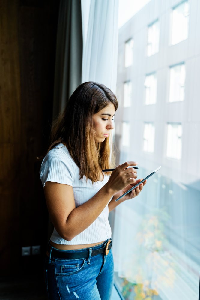 A woman uses a digital pen on a tablet indoors