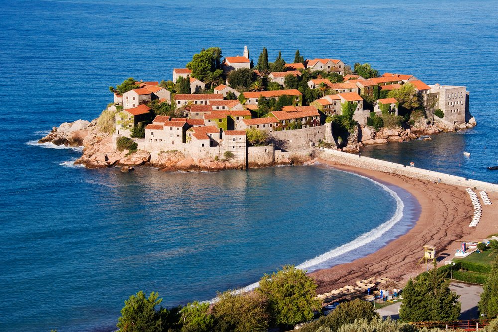 Historic Sveti Stefan island village with stone buildings and red tile roofs.