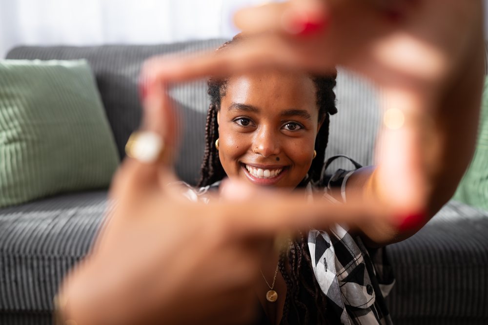 A young woman smiles while framing her face with her hands on a couch in a living room, moving, Spain.