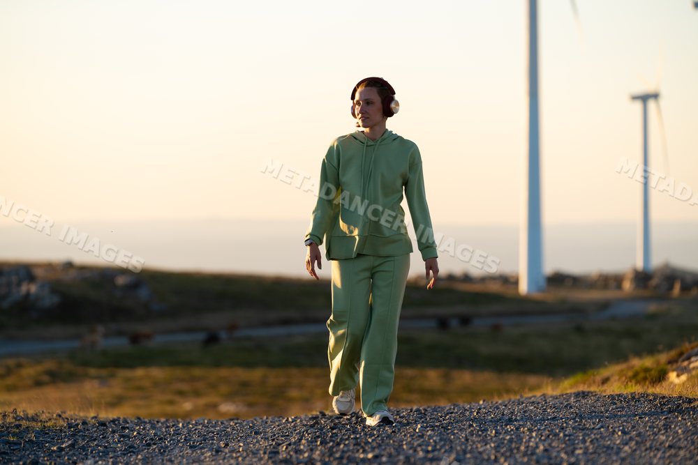 A white woman walks near wind turbines at sunset in Galicia, Spain