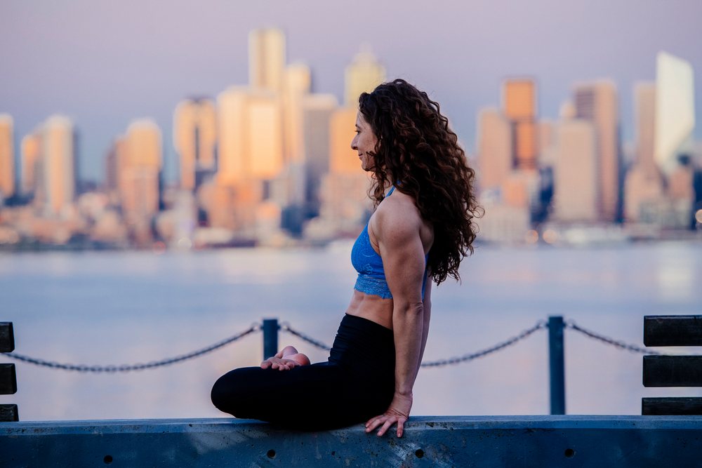 Woman practicing seated yoga pose outdoors by the waterfront with Seattle cityscape in the evening, WA, USA.