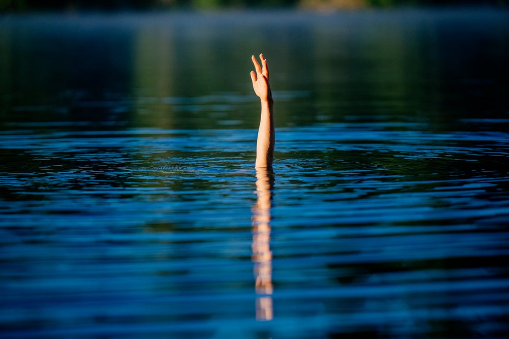 Hand raised above the surface of a still lake water, creating ripples and reflection, USA.