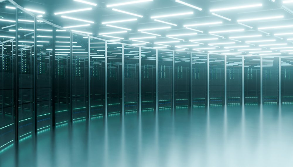 Interior of a data center with rows of illuminated server racks and reflective flooring.