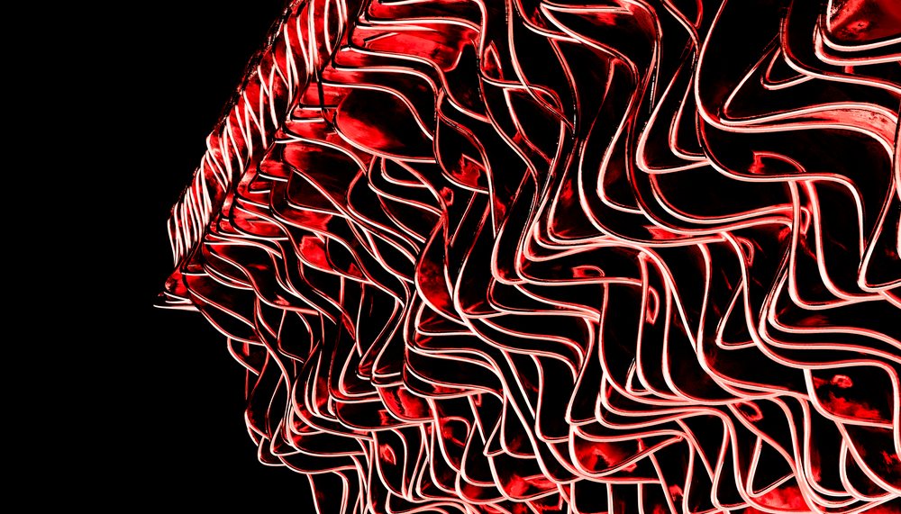 Abstract folded metal sculpture illuminated with red lighting against a black background.
