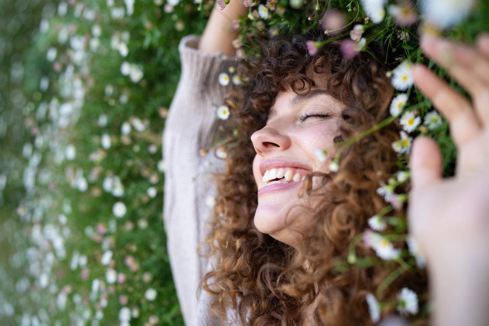 Woman with curly hair smiling and lying in a field of daisies enjoying a peaceful spring day outdoors, home story, influencer, Spain.
